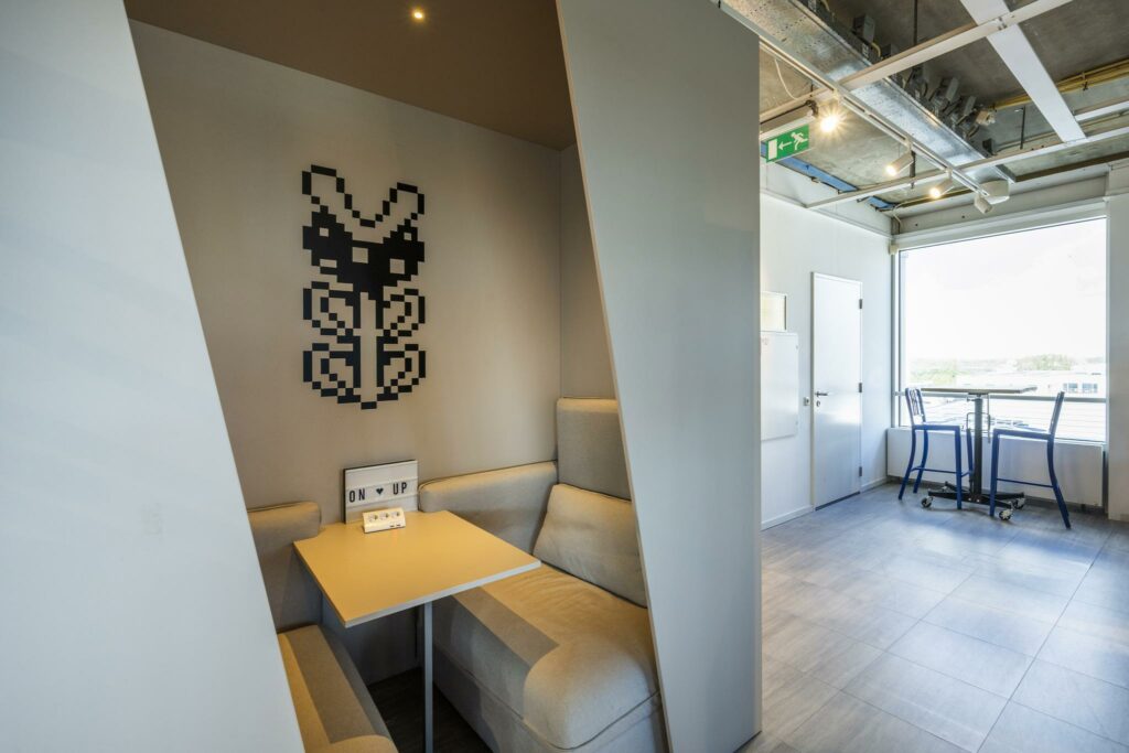 Moderne zithoek met grijze banken, een tafel en pixelkunst aan de muur in een kantoor aan de Johan Huizingalaan.